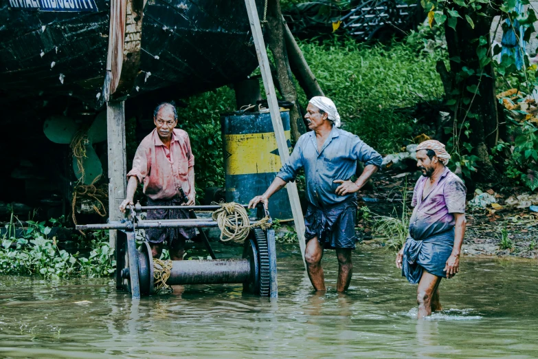 three people walking through a muddy body of water