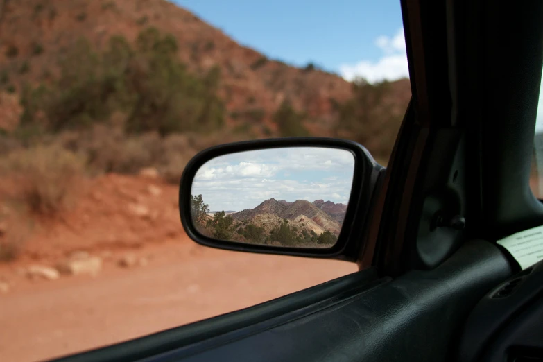 a side mirror reflecting a mountainside and trees