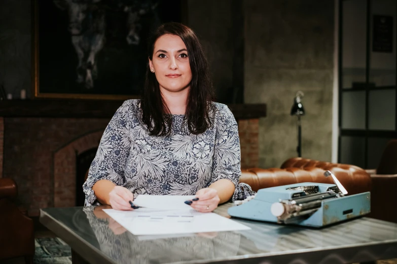 a woman with a pen and paper sits at a desk