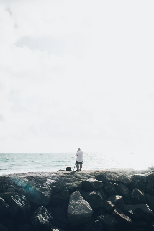 two people are standing on a rocky beach by the ocean