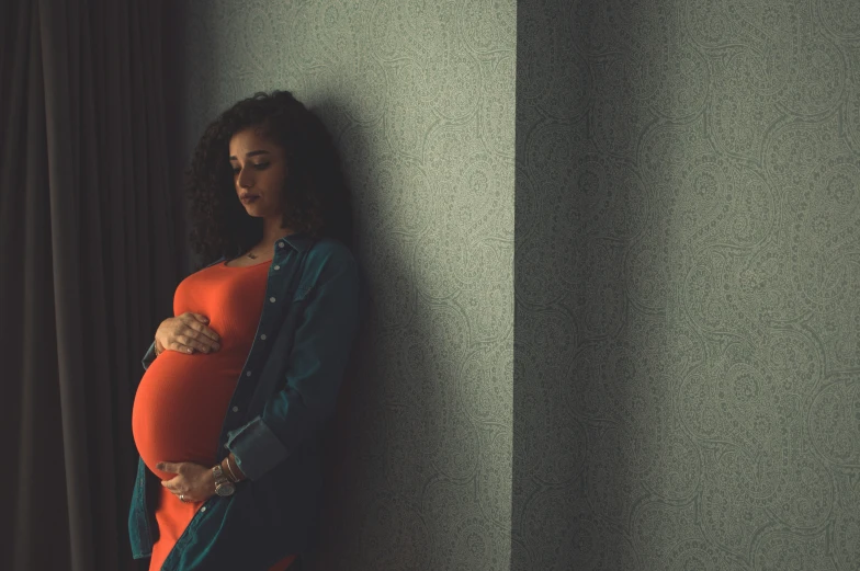 a young pregnant woman leaning against a wall