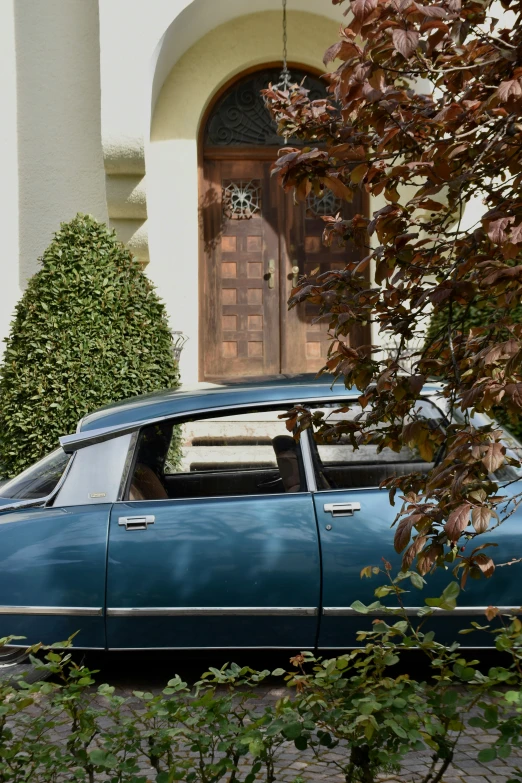 an old blue car sits parked next to a house