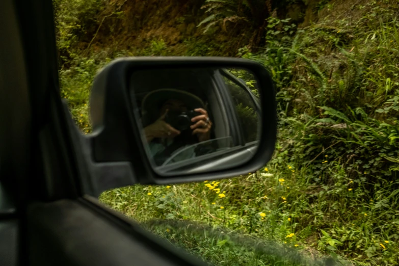 a car's side view mirror is in front of a woman taking her picture of herself through it