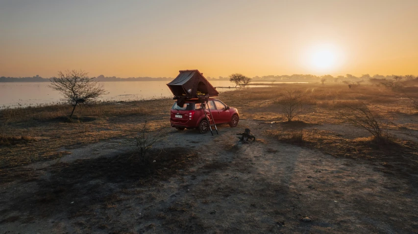 a red car parked by the lake at sunset