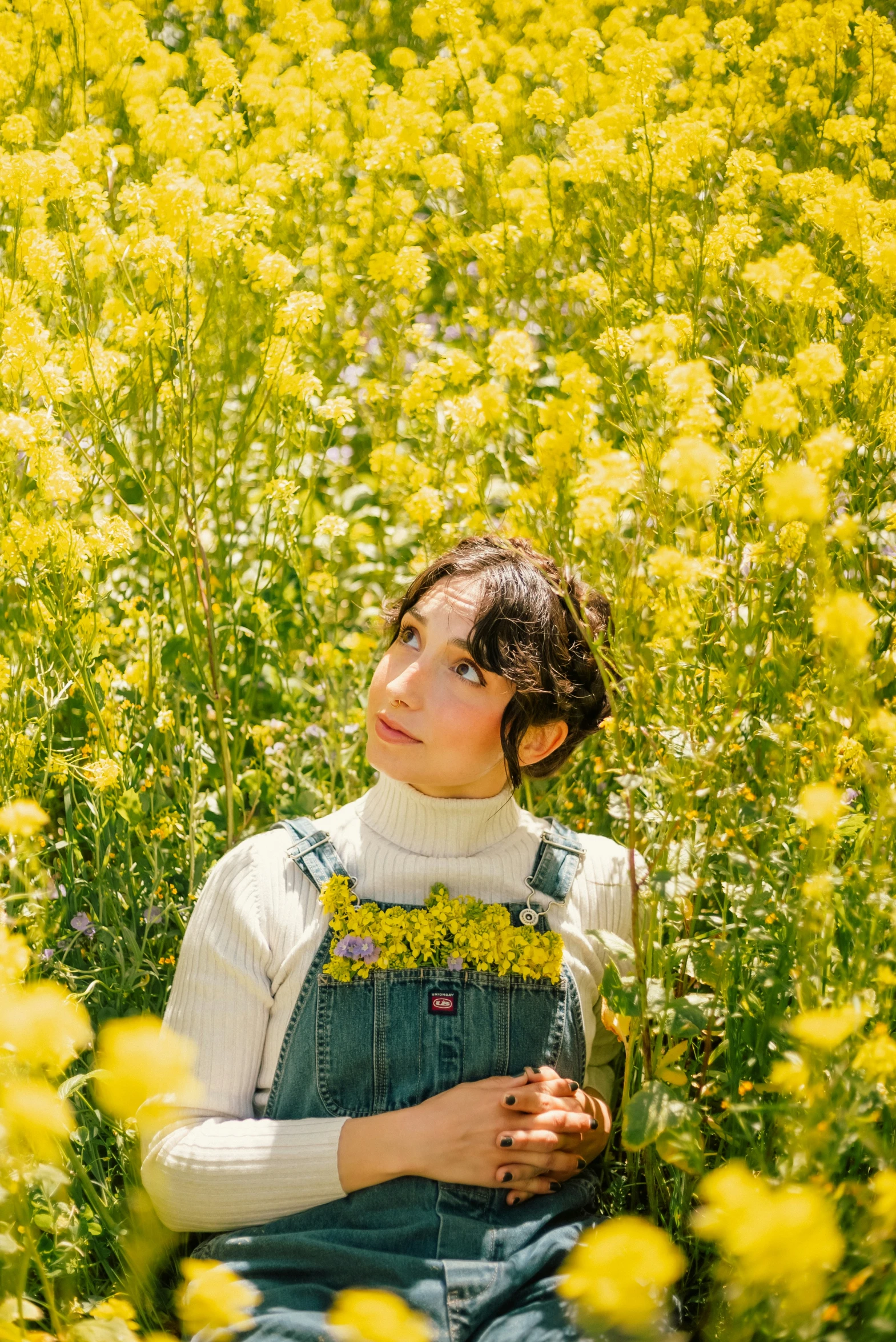 a girl wearing overalls sitting in a field of flowers