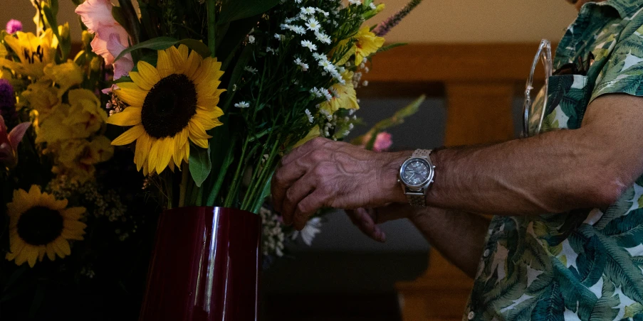 a man with watch, holding flowers and another man looking at it