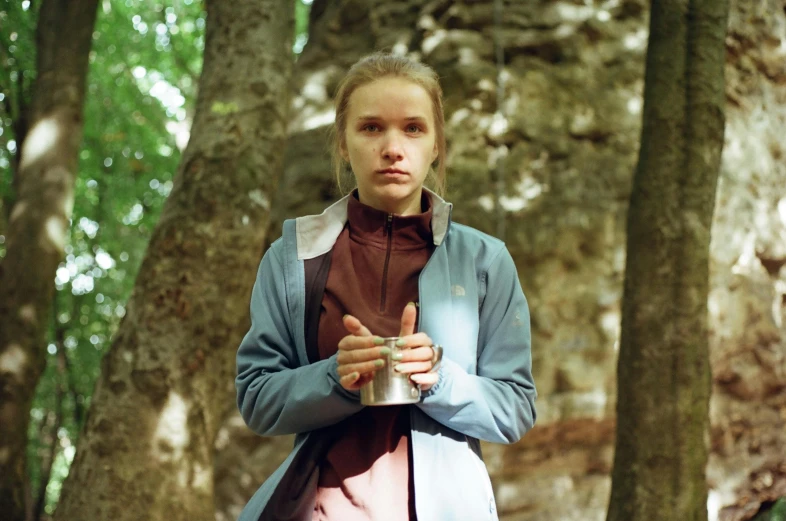 a young lady is holding a glass of water in the woods