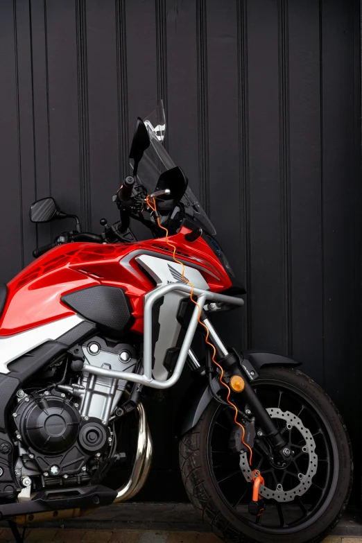 the red motorcycle is parked by a black wall