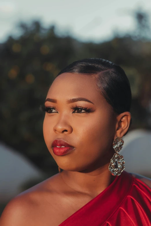 a woman wearing statement earrings and a red one shoulder dress