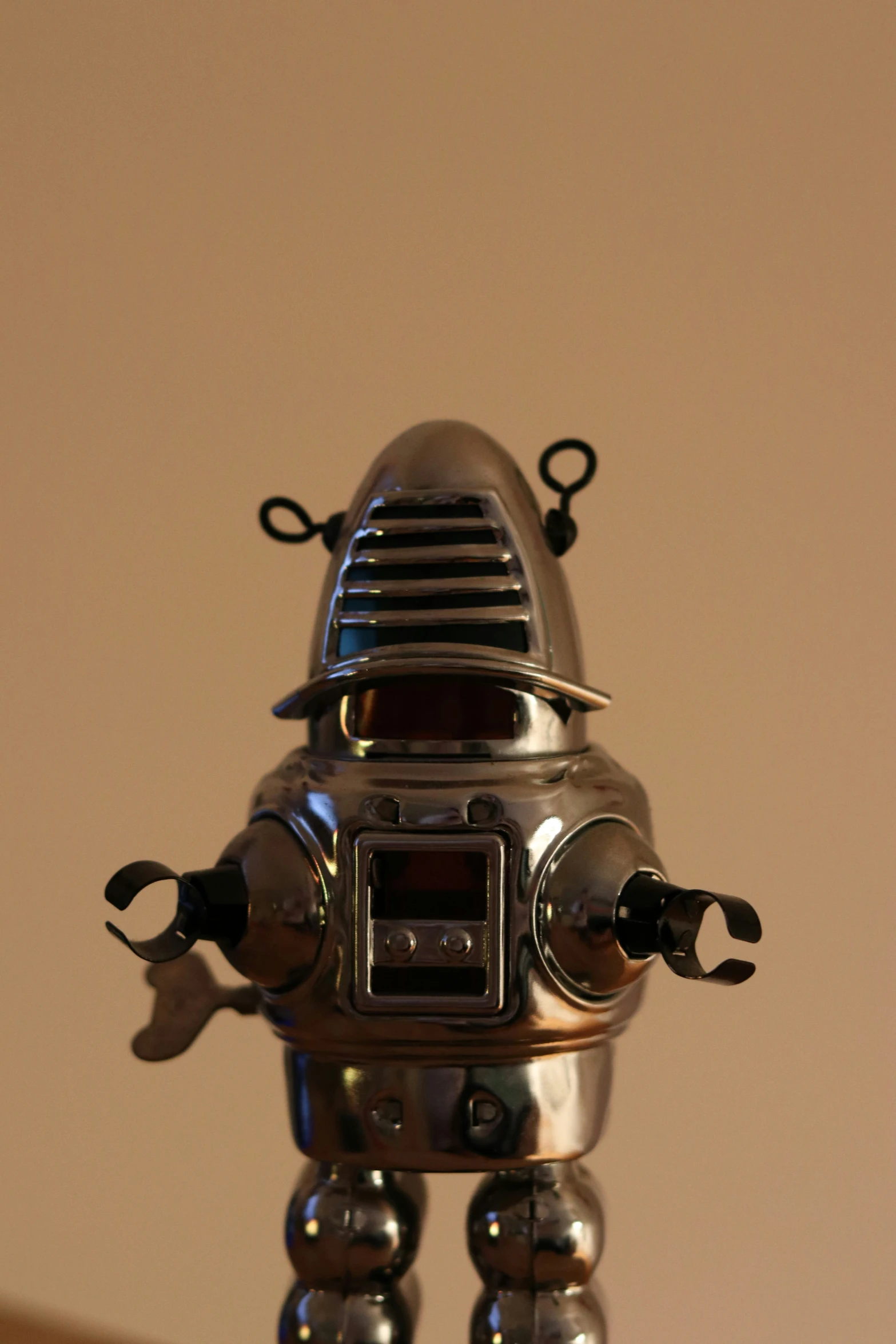 a metal robot is on a shelf in front of a beige background