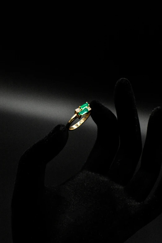 a hand holding an ornate gold ring with green stones