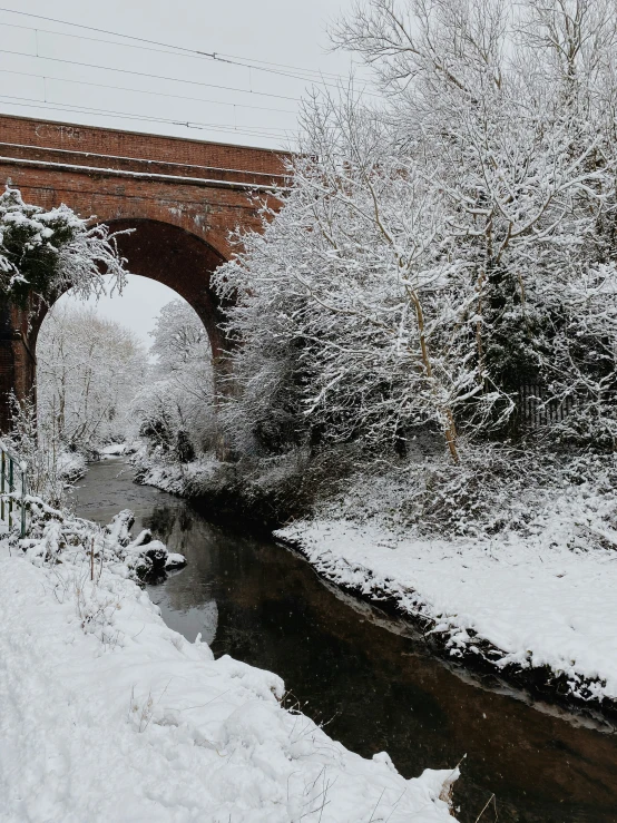 snow covered trees and river below an old red brick bridge