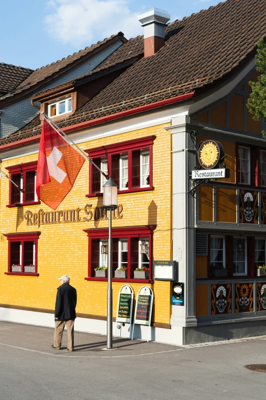 a man standing in front of a yellow building with a flag