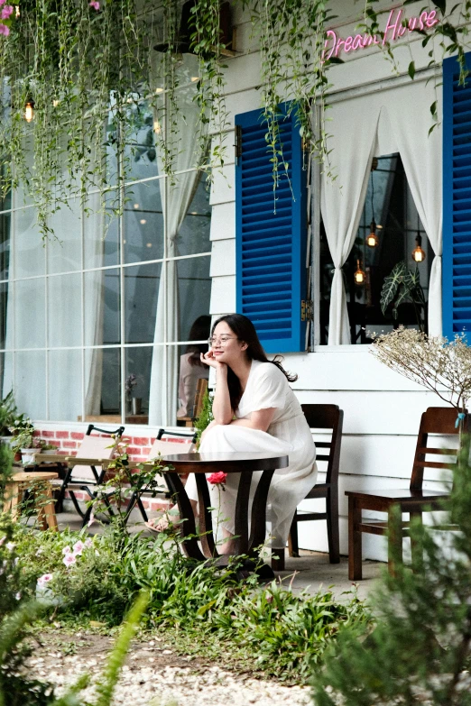 a girl sitting at a table outside in front of the window