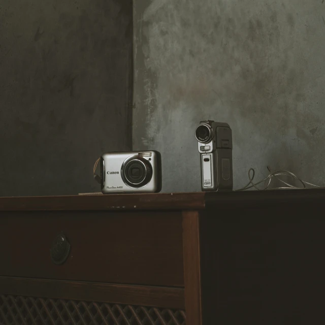 two cameras are on a wood dresser top