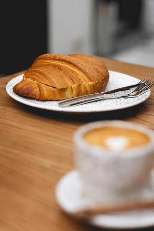 a croissant is on a white plate with a fork next to a cup