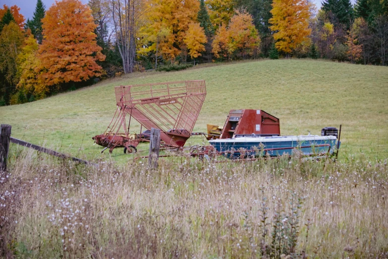 a rusted old boat is in a field next to a fence