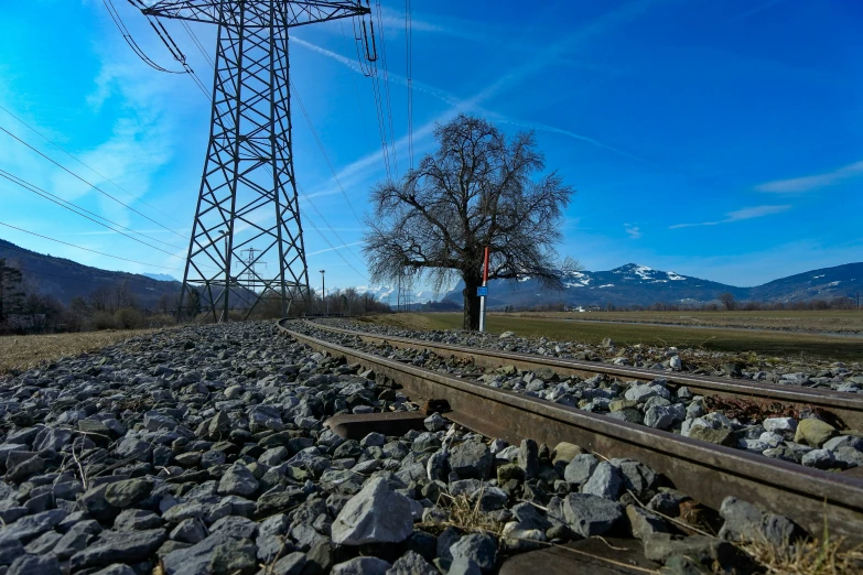 a train track with power lines and a lone person standing under the poles