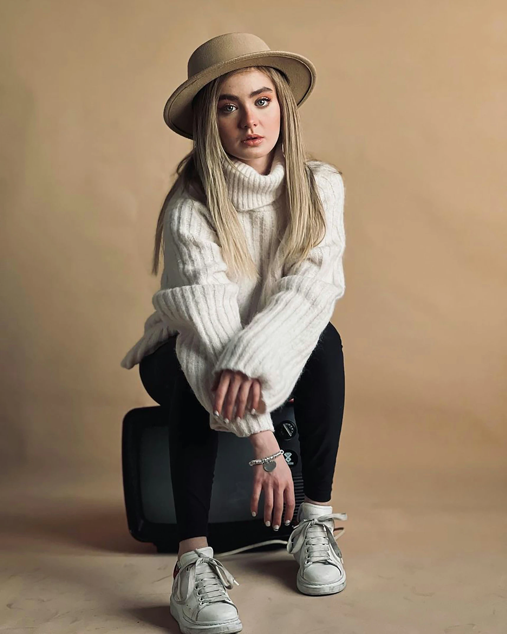 a person posing for the camera wearing a hat, sweater and sneakers