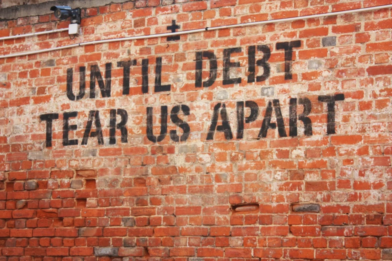 an image of a sign that says until debt tears apart on a brick wall