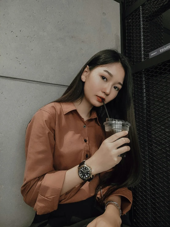 the woman sitting in front of a wall drinking soing out of a glass