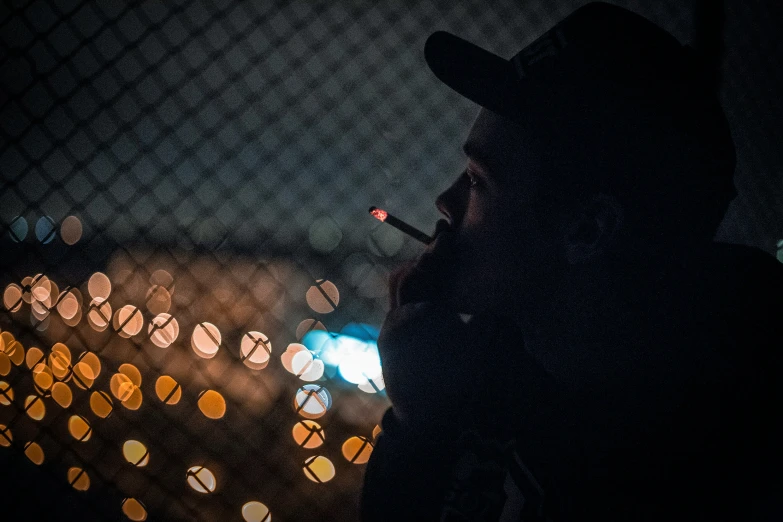 a man in a hat stands next to a fence at night