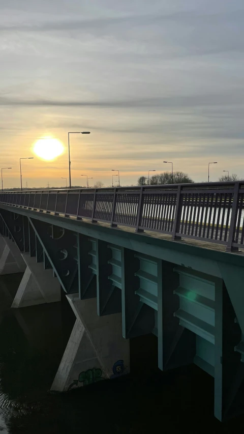 the sun is rising over a bridge with a reflection on the water