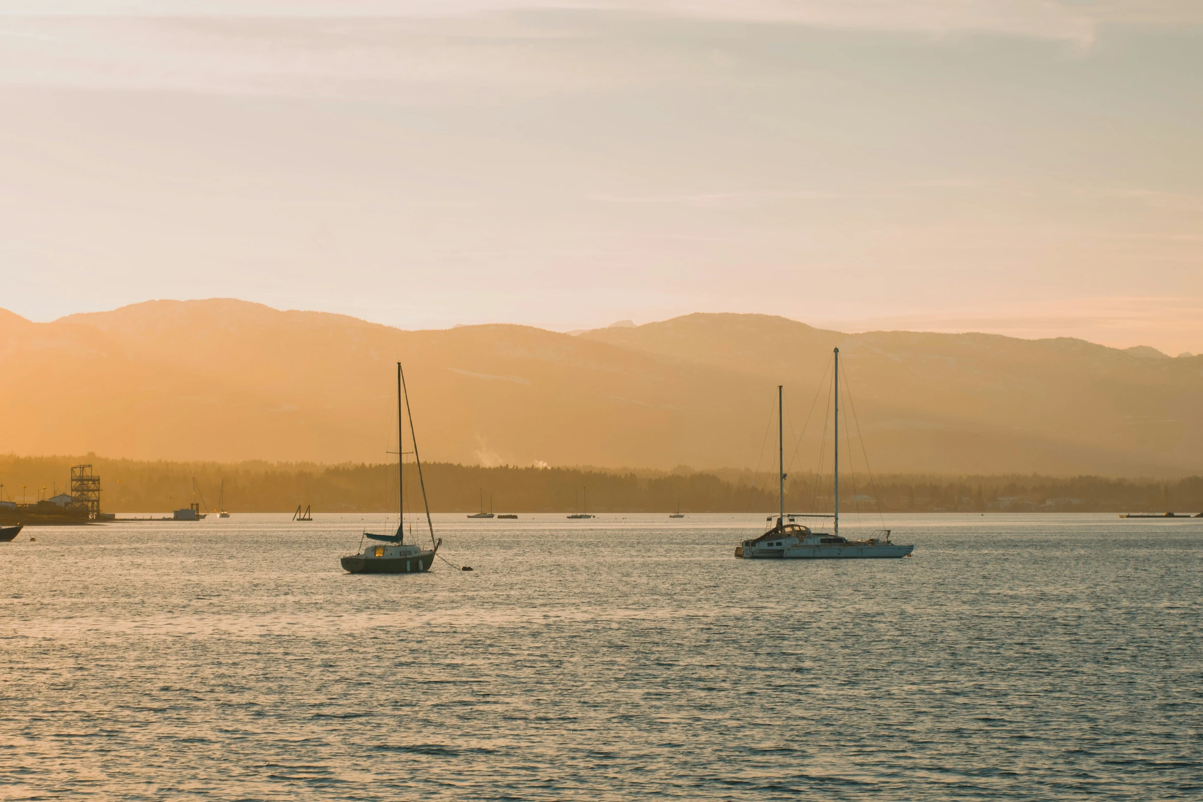 three sailboats sitting out in the water, with mountains behind them