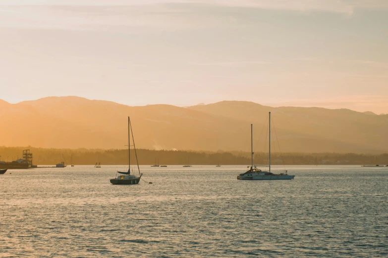 three sailboats sitting out in the water, with mountains behind them