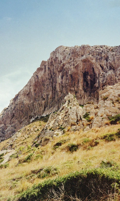 a rock face sits on the side of a grassy hill