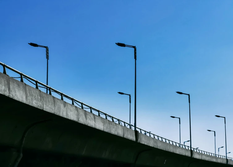 multiple street lamps on either side of a long cement wall