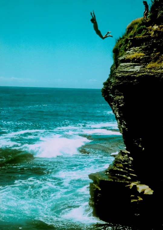 a person is diving off the side of a cliff