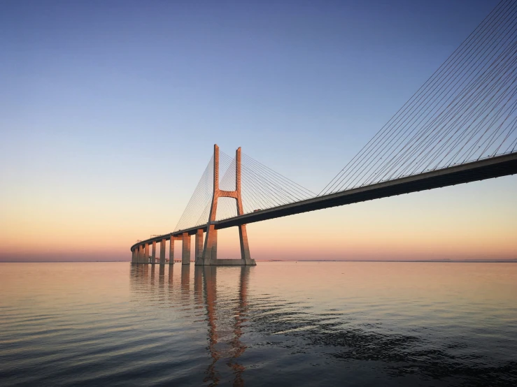 a long bridge is spanning the water towards the sunset