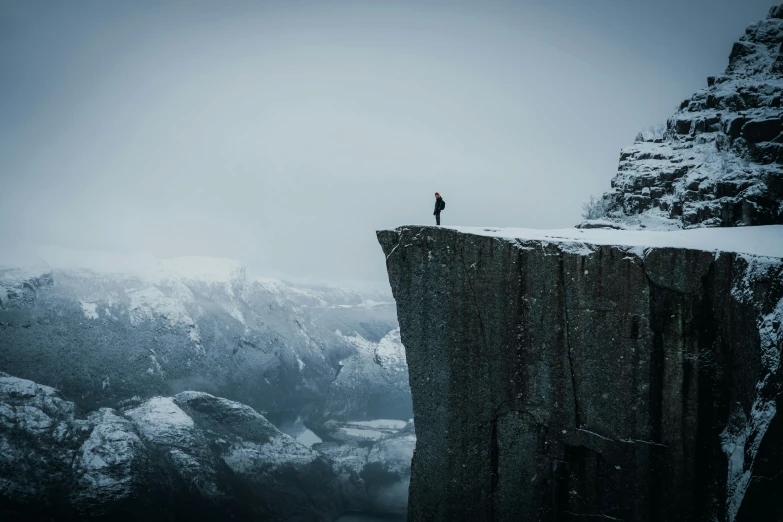 the lone man stands at the top of the edge of a high cliff