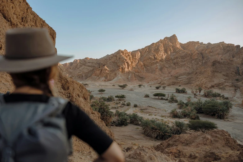 man in hat standing on top of a mountain overlooking a valley