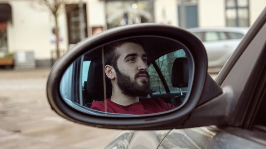a reflection in a side view mirror of a bearded man
