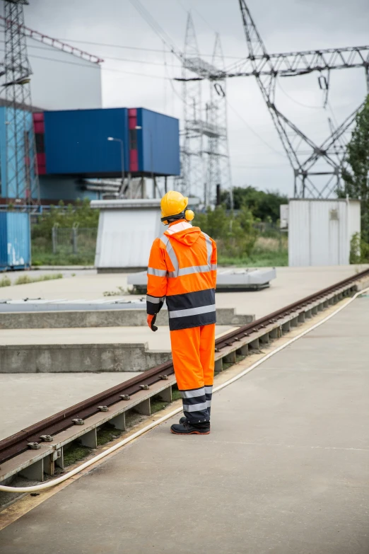 man in orange safety suit standing on rail road tracks