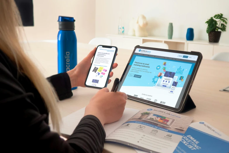 a person uses their cell phone while looking at a laptop on their tablet