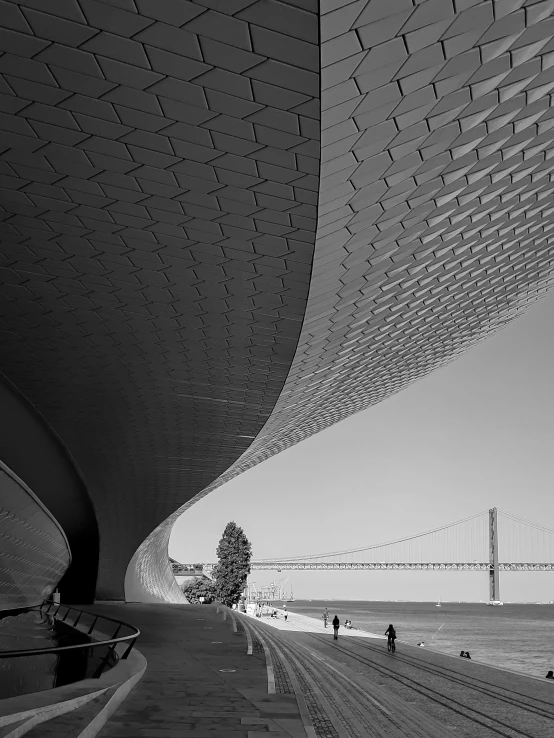 people walking on a concrete walkway underneath a large suspension bridge