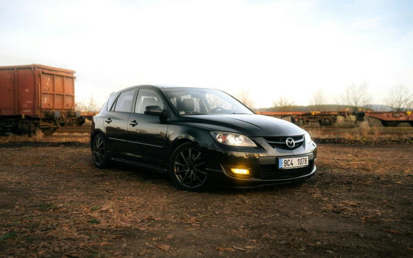 a black sedan parked on dirt near train cars