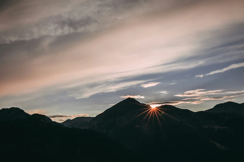 a mountain landscape with clouds and the sun