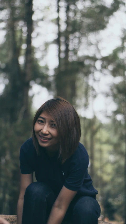 a smiling young woman crouching on a rock in the woods