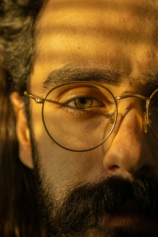 closeup of a man's eye and beard wearing gold glasses