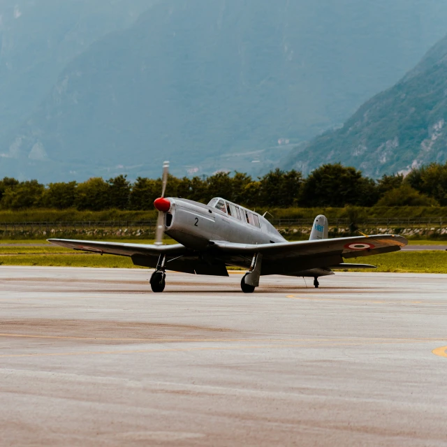 small grey airplane sitting on tarmac with mountains in background