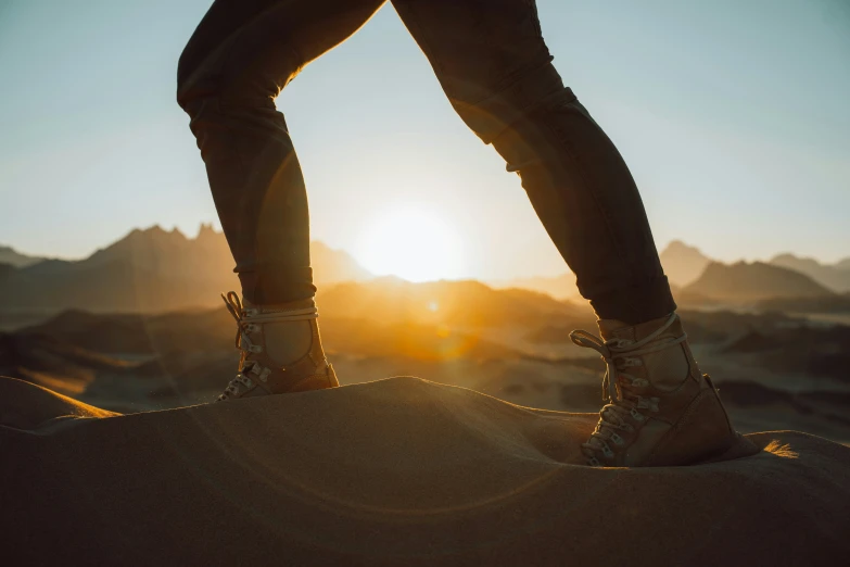 legs with hiking boots standing on sand with mountains in background