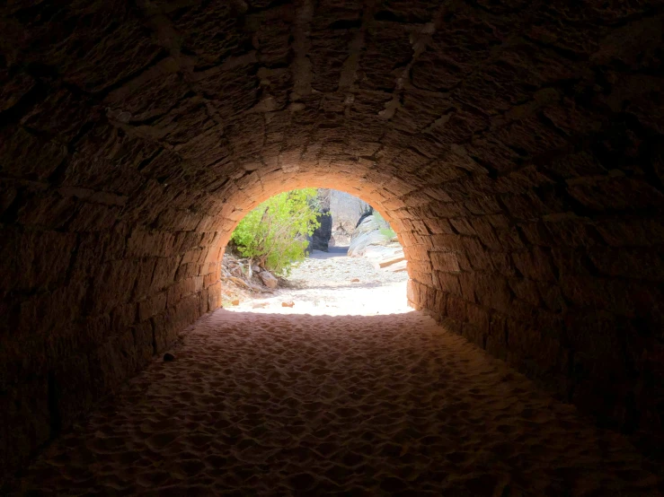 dark, light tunnel with small stones and trees in the background