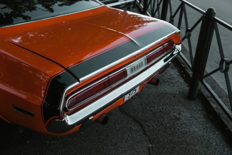 an orange muscle car parked next to a fence