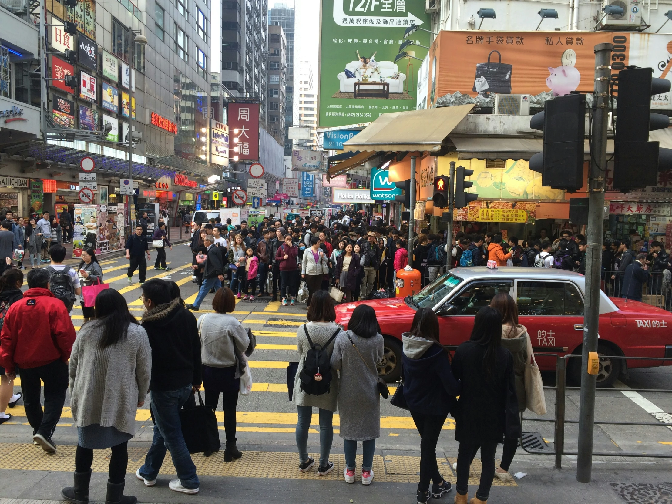 a crowded city street has a red car passing by