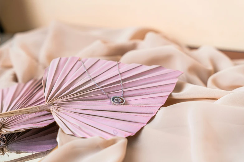 a paper fan laying on a blanket next to a small necklace