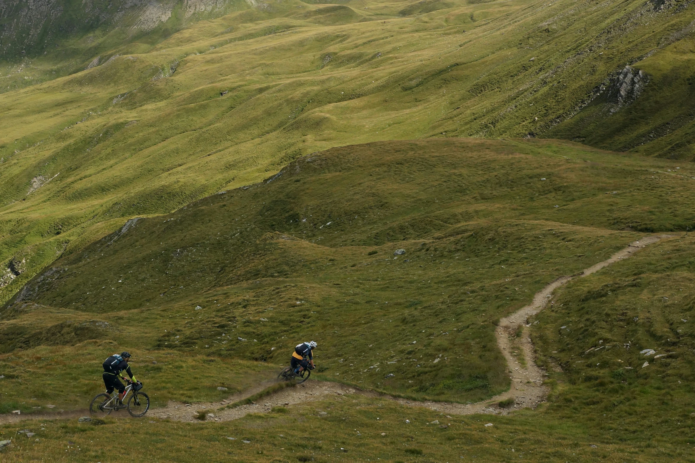 two people riding mountain bikes uphill on grassy hillside